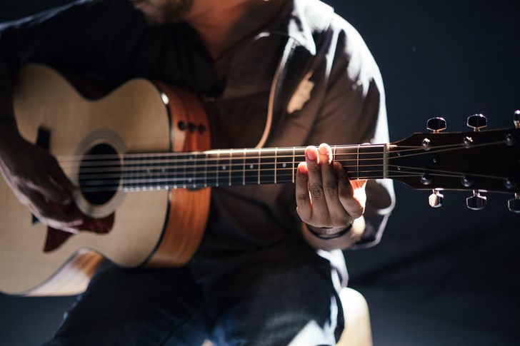 Man sitting on a stage playing guitar.